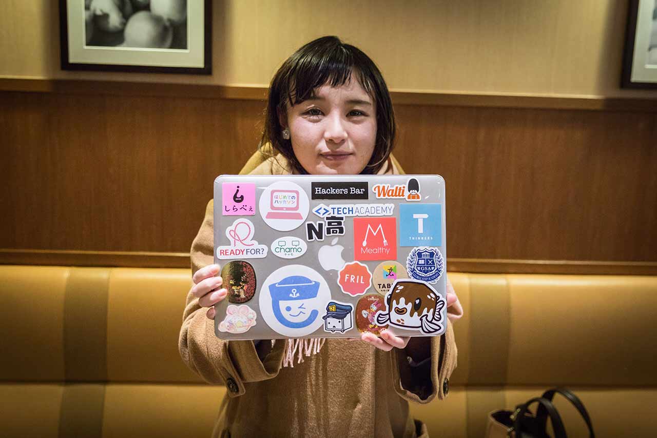 NEET Rental Mio holding up her laptop with the Tofugu sticker on it