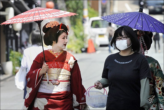 Japanese woman in a surgical mask walking with two geishas