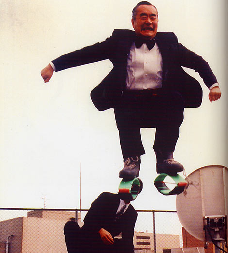 Dr. NakaMats jumping into the air with spring-like contraptions stuck to his feet