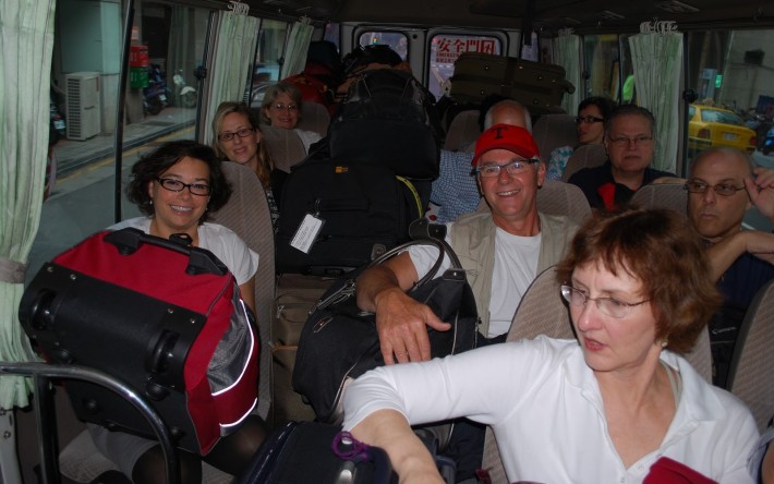 Tourists on a bus with bulky luggage on their laps and other seats