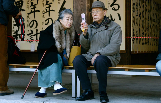 Elderly couple sit on a bench and use their cellphone