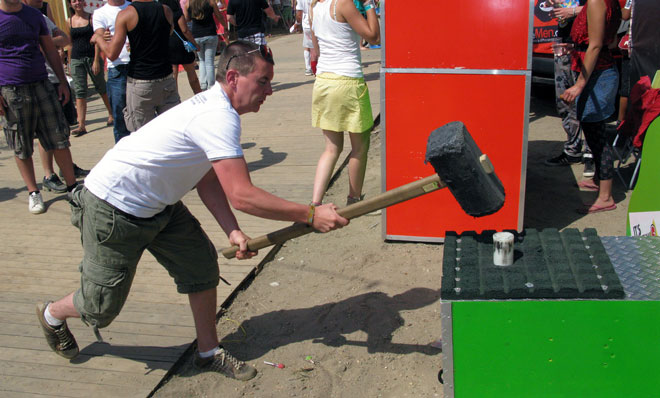 Man at a carnival bringing a large hammer down on a peg