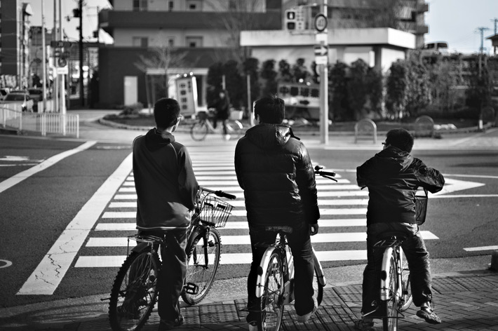 three kids on bicycles waiting to cross the street