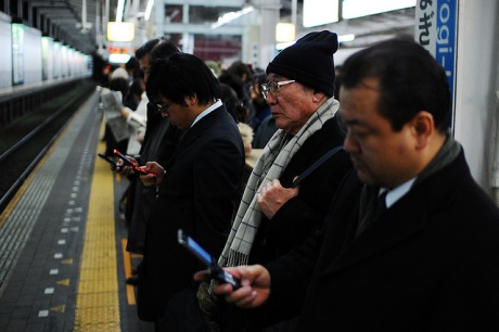 Japanese people lined up in the subway, looking at their phones