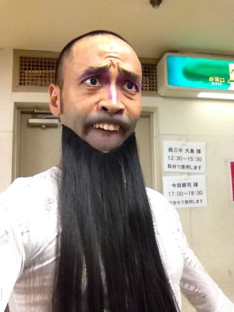 Japanese man makes a weird face while wearing a fake beard and showing his teeth