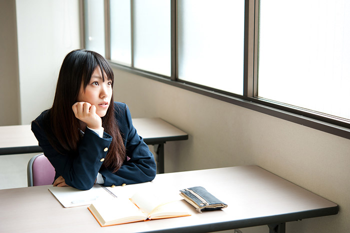 asian student sitting at desk in school with notebook