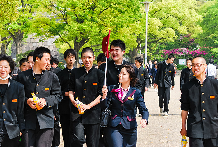 class of japanese students in uniforms following a tour guide