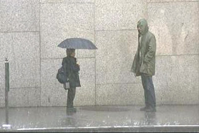 man standing in the rain looking at a kid holding and umbrella