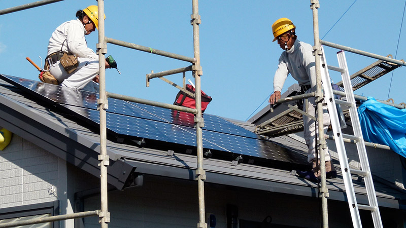 Construction workers installing solar panels on a house