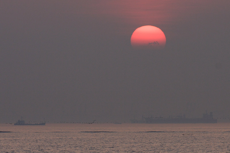 Red sun setting over a hazy sea