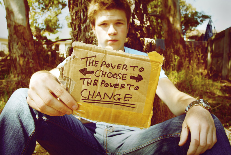 boy sitting at tree and holding sign