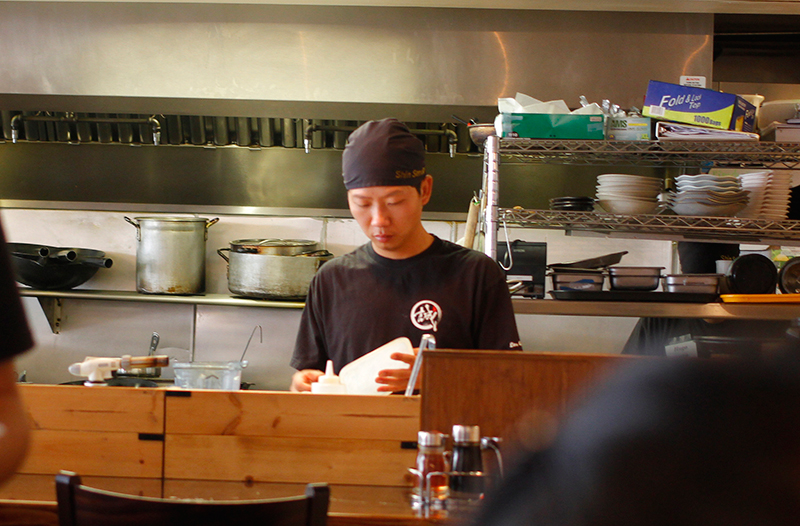 man in black making ramen at a wooden counter