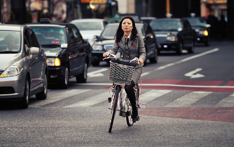 Japanese woman in grey suit riding bike with basket