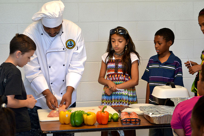 navy chef prepares food with elementary school students