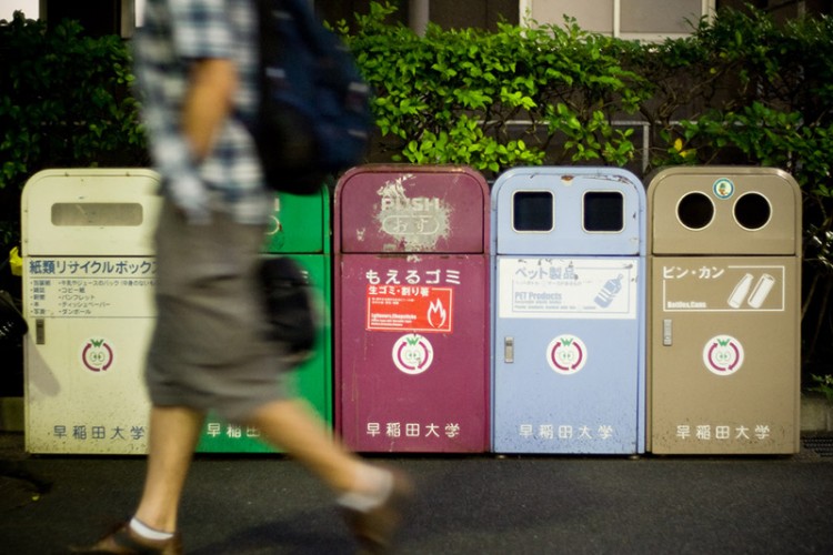 A man walks by five Japanese garbage bins