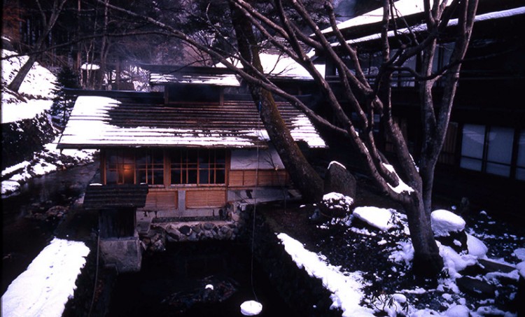 A wooden Japanes-style building by a pond in the snow