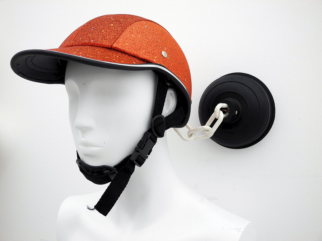 a chindogu hat with a chain attached to a plunger stuck to a wall