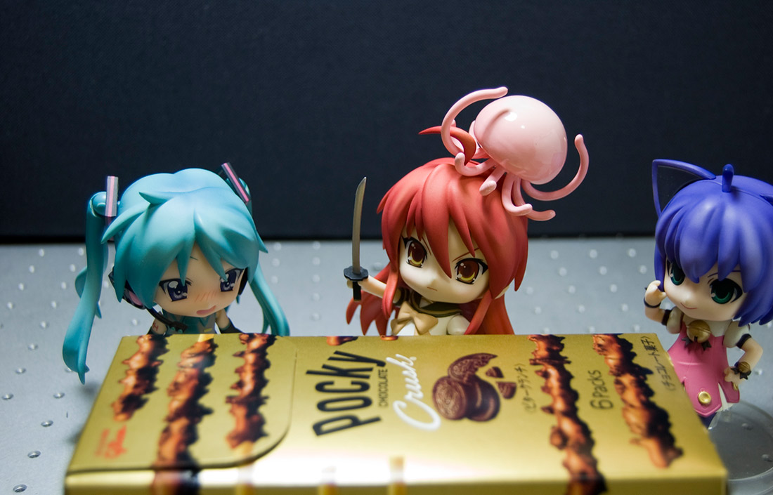 small anime figures surrounding a box of pocky