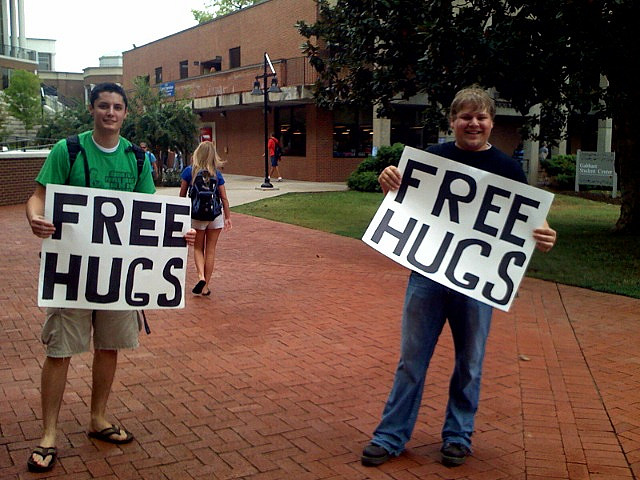 students on campus holding signs that say free hugs