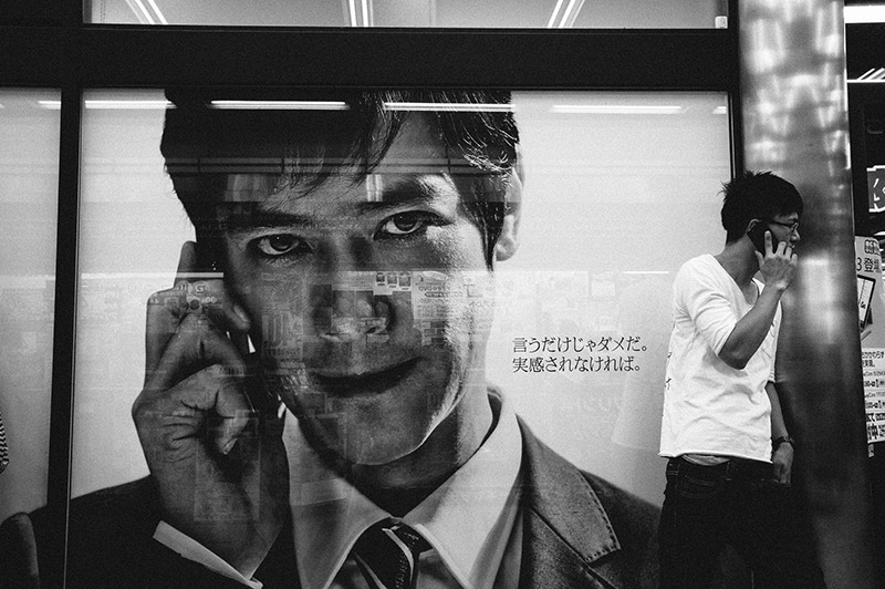 A man on a cell phone in front of a large ad of a man on a cell phone