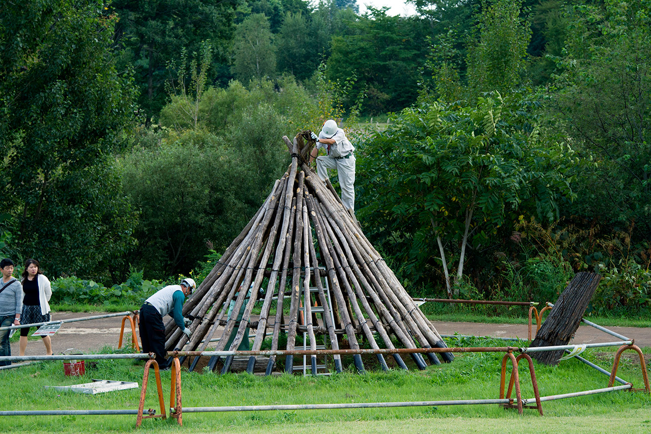 onlookers watch two men build hut