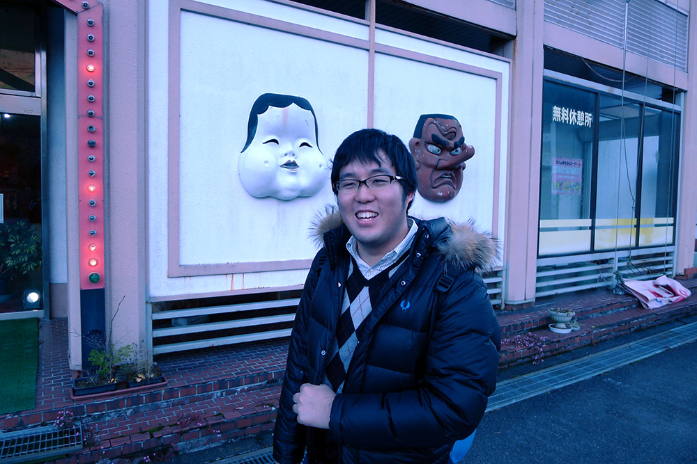 man standing smiling in front of a building with japanese masks