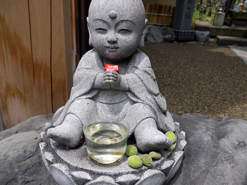 japanese stone shrine statue jizo with chocolate and plums