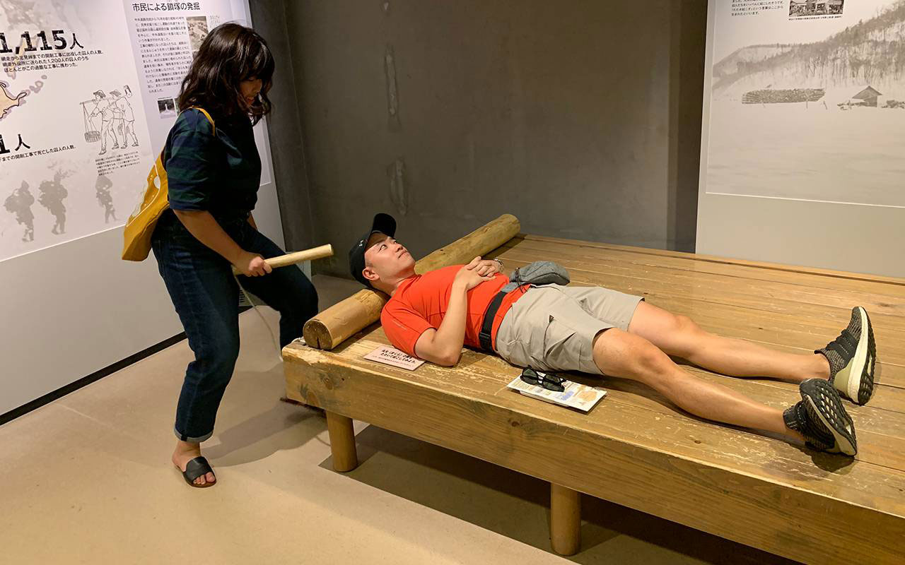 Museum visitor experiencing being woken up by someone banging on the wooden pillow